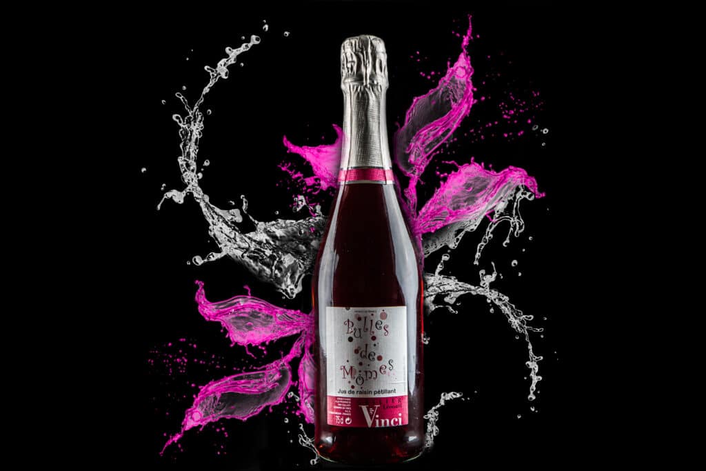Jus de Raisin Pétillant Bulles de Mômes - Cellier de Vinci Bouteille de jus de raisin pétillant Bulles de Mômes, éclaboussures dynamiques roses et blanches sur fond noir.