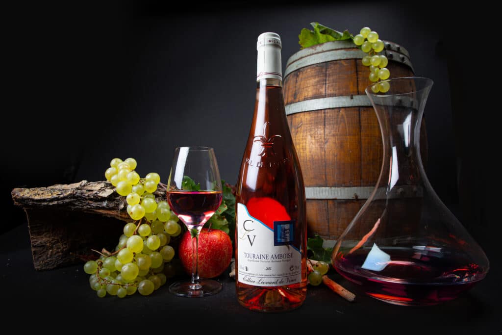 Vin Rosé Touraine Amboise et Cellier Léonard de Vinci Bouteille rosé Touraine Amboise Cellier Léonard de Vinci, raisins et carafe devant un tonneau en bois.